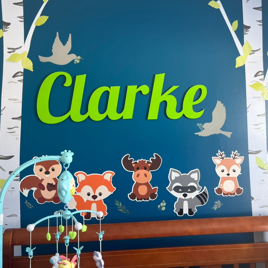 Children's room decor with name 'Clarke' on a blue background, featuring animal illustrations and a mobile.