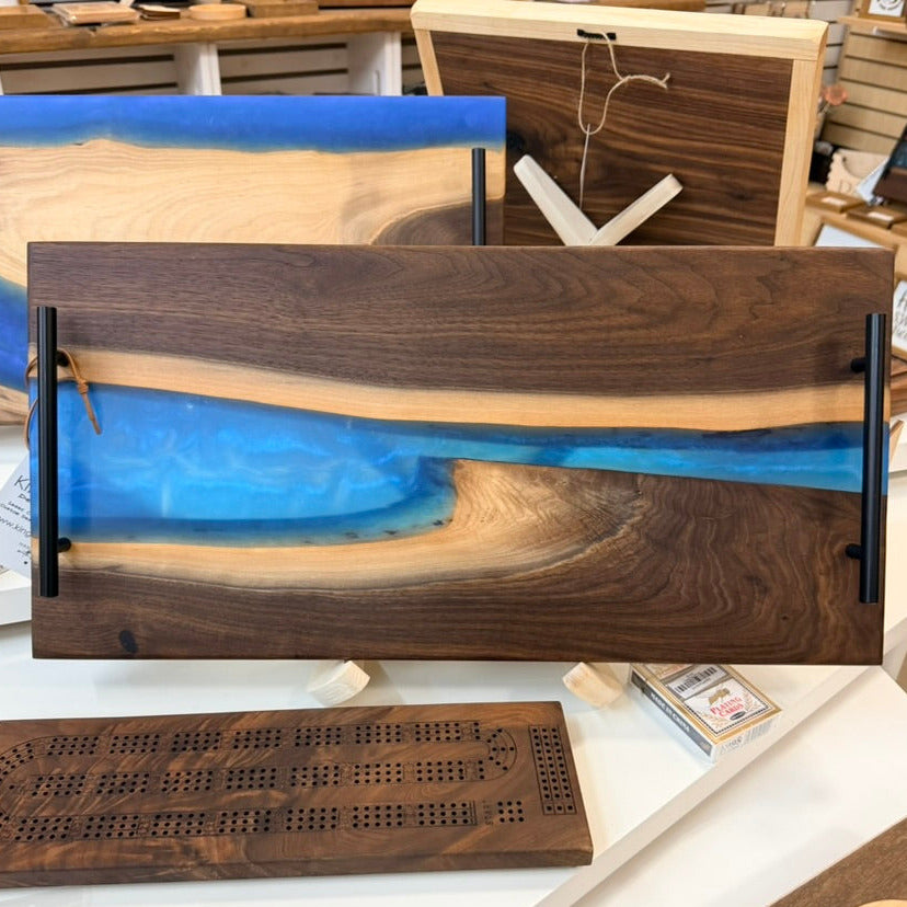 Wooden cribbage board with blue resin inlay on a display table.
