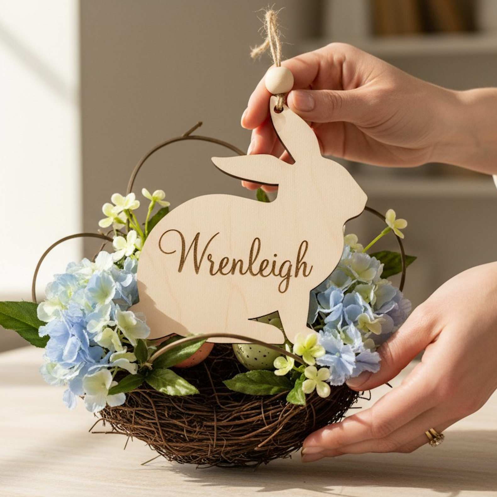 Hand holding a wooden bunny-shaped sign with 'Wrenleigh' on a floral arrangement.