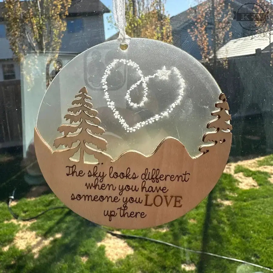 Decorative hanging ornament with trees, heart, and quote on a blurred outdoor background
