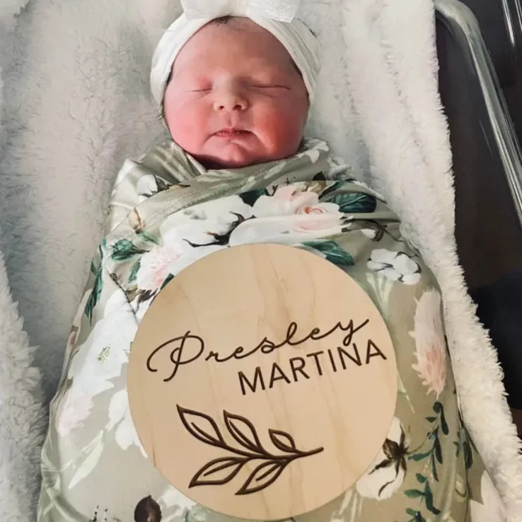 Newborn baby swaddled in floral blanket with natural birchwood unique grain product